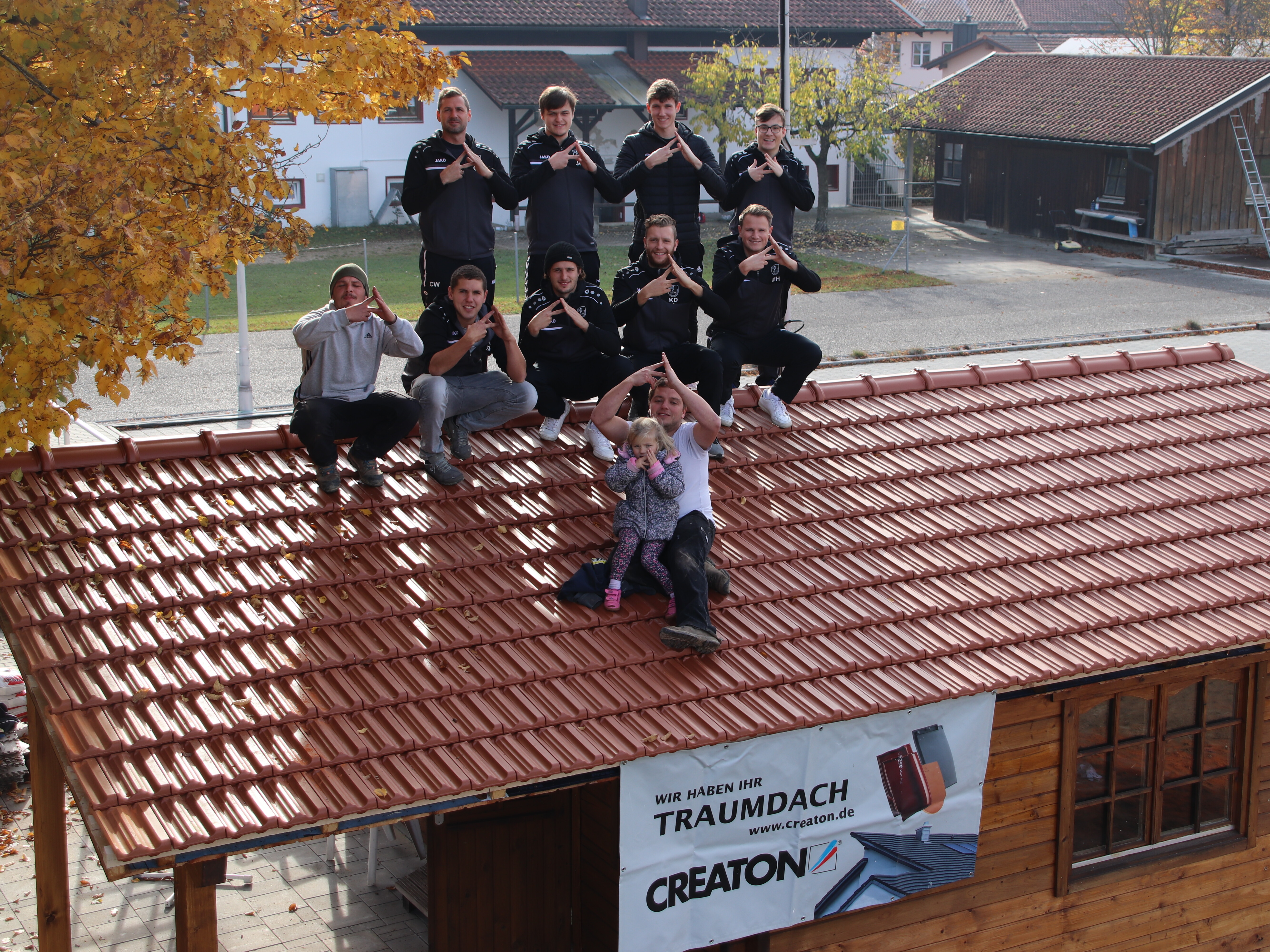 Ein Teil der Fußballmannschaft des TSV Obertaufkirchen und von Holzbau Tröstl zeigen die Dachgeste auf der neu eingedeckten Verkaufshütte des Fußballvereins. Mit diesem Bild gewannen der TSV sowie das Unternehmen die 1000 € Spendensumme im letzten Quartal 2021.